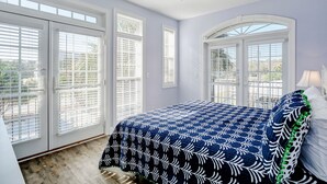 A bedroom with a bed, a ceiling fan, and large windows with blinds.