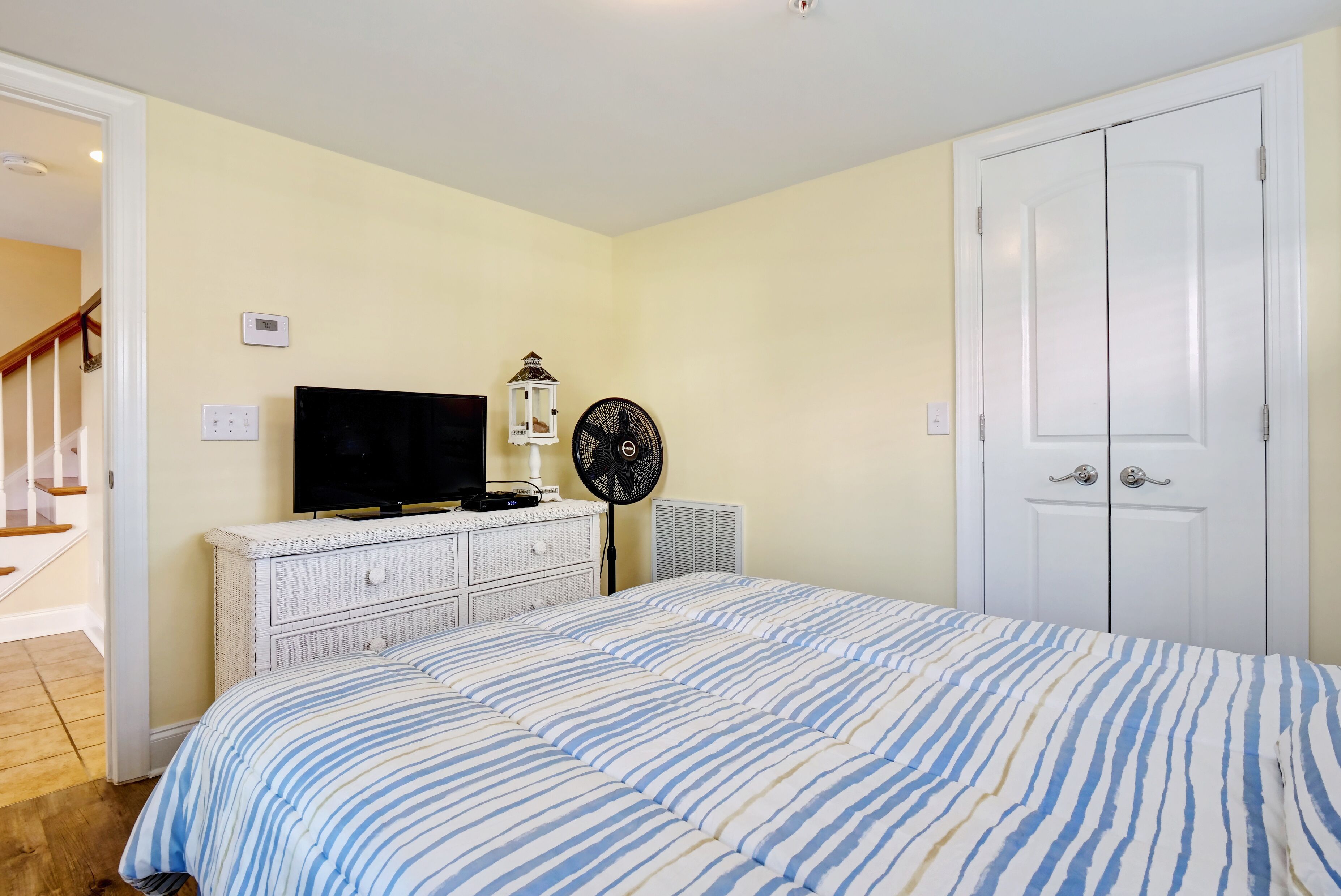 A bedroom with a bed, dresser, TV, fan, and a white door.