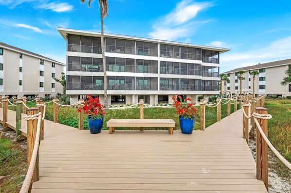 Un hotel moderno con una estructura de varios pisos, una terraza de madera con un banco y flores rojas en macetas.
