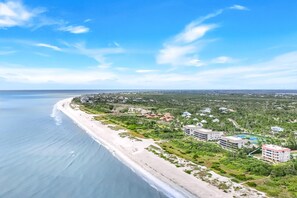 Vista aérea de un complejo turístico frente a la playa, con varios edificios y abundante vegetación.