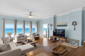 Enjoy ocean views from the comfort of this living room, featuring a large TV, dining table, and comfortable seating.