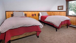 Une chambre avec deux lits en bois, chacun recouvert d’une courtepointe rouge et agrémenté d’oreillers à rayures.