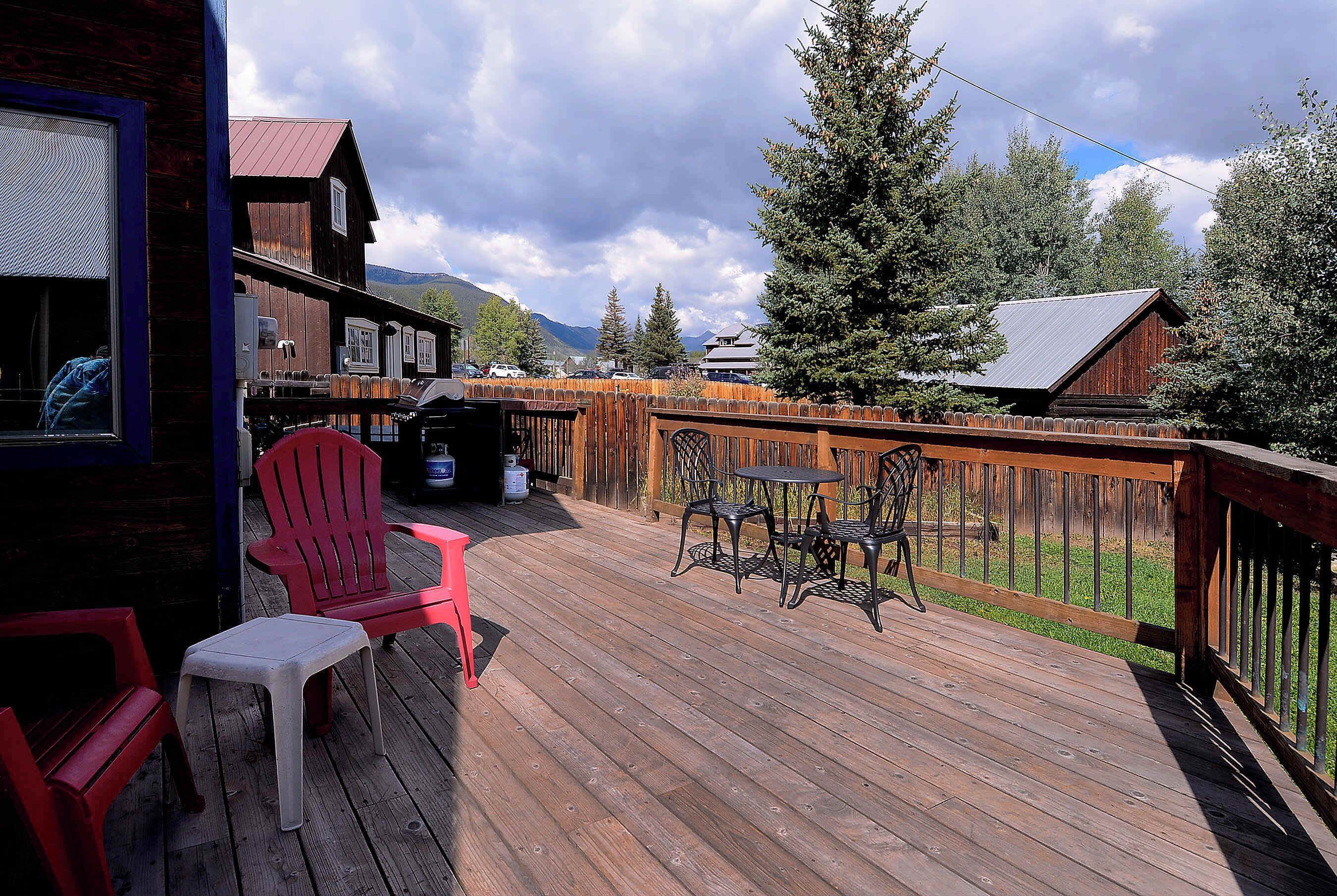 A wooden deck with outdoor seating, a red chair, and a white chair.