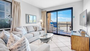Un soggiorno moderno con divano, tavolino e televisore. È presente un balcone con mobili da esterno.