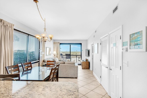A modern living room with a glass dining table, a sofa, and a balcony with a view.