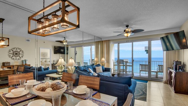 A spacious living area with a dining table set for a meal, a blue sofa, and a balcony with a view of the ocean. - 🌴Beach Chairs~Gulf Views~2 Pools~Leeward Key 905~Suite Sea-Cret🌴 (Miramar Beach)