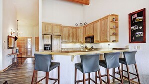 Una cocina con armarios de madera, una isla central con taburetes de bar, un microondas y un refrigerador.