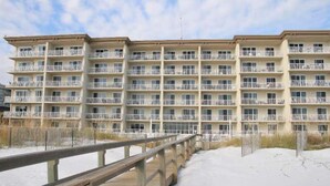 A multi-story hotel with balconies, a wooden deck, and a sandy beach in the foreground. - Summer Place #204 - 3 BR Beachfront Condo - Free Beach Service! (Fort Walton Beach)
