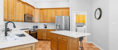 A kitchen with wooden cabinets, a stainless steel refrigerator, a microwave, and a sink.