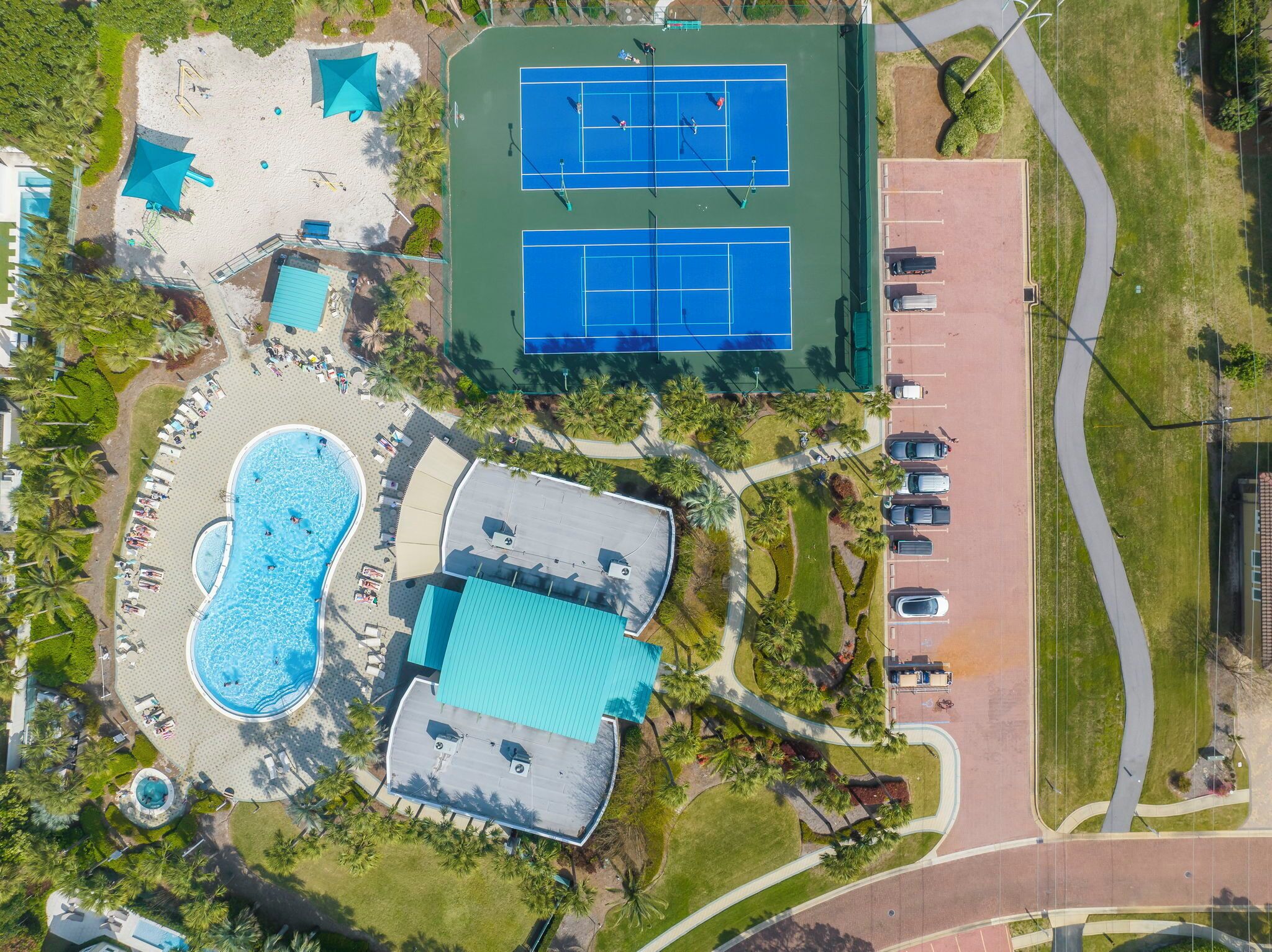Oversigtsbillede af et resort med swimmingpool, tennisbaner og parkeringsplads.