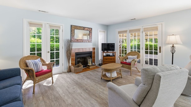A living room with a fireplace, television, wicker furniture, and large windows.