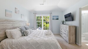 A bedroom with a bed, a ceiling fan, a TV, a dresser, and a window with curtains.