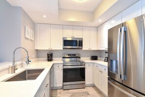 A modern kitchen with white cabinetry, stainless steel appliances, and a built-in oven. - Updated, modern, beachfront condo w/private balcony! 🌴 (Destin)