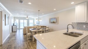 A kitchen with a marble countertop, stainless steel sink, and a dining area with a wooden table and chairs.
