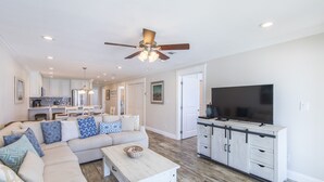 A spacious living room with a large sofa, a coffee table, and a TV in the adjacent kitchen area.