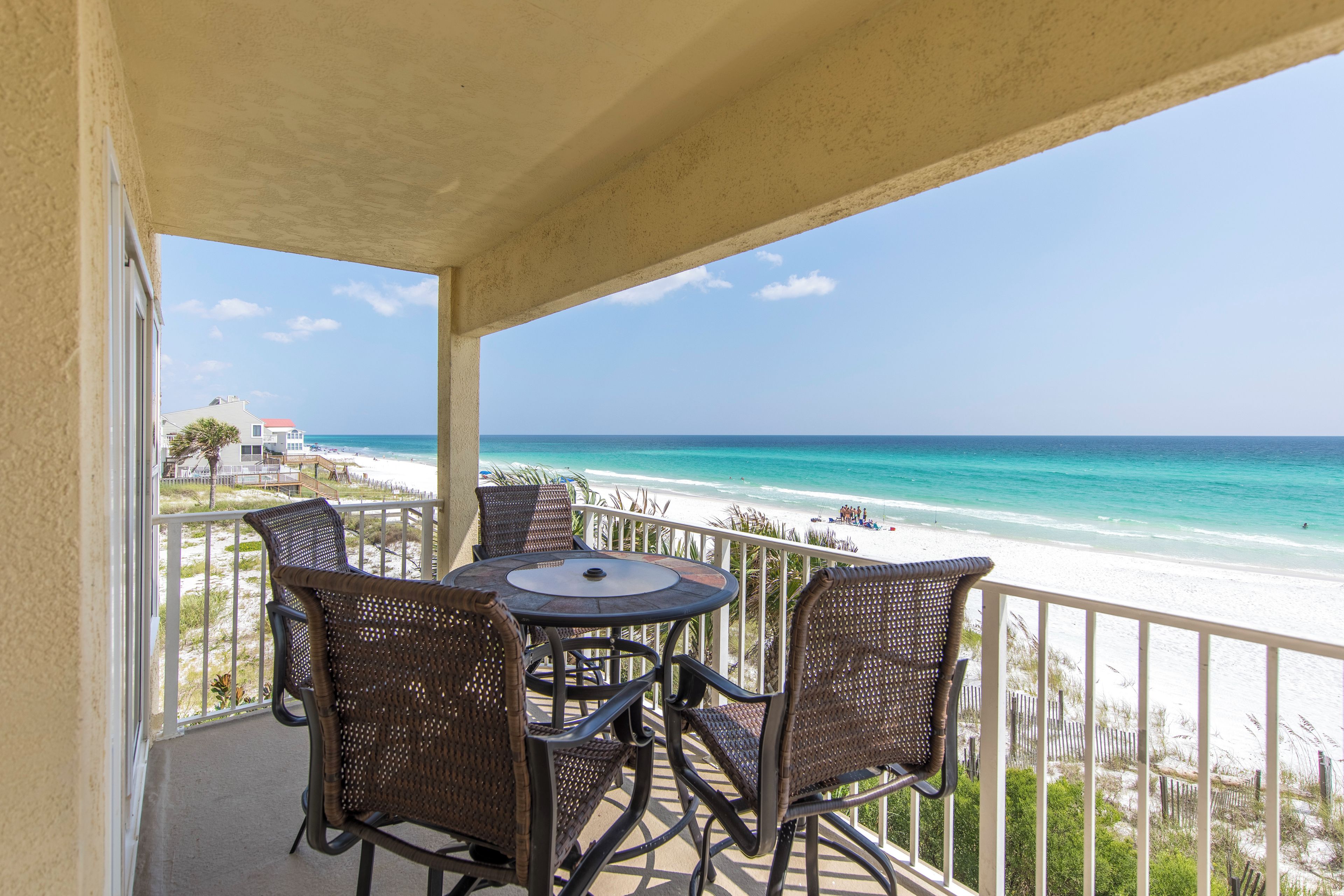 A balcony with wicker chairs and a table overlooking a beach.