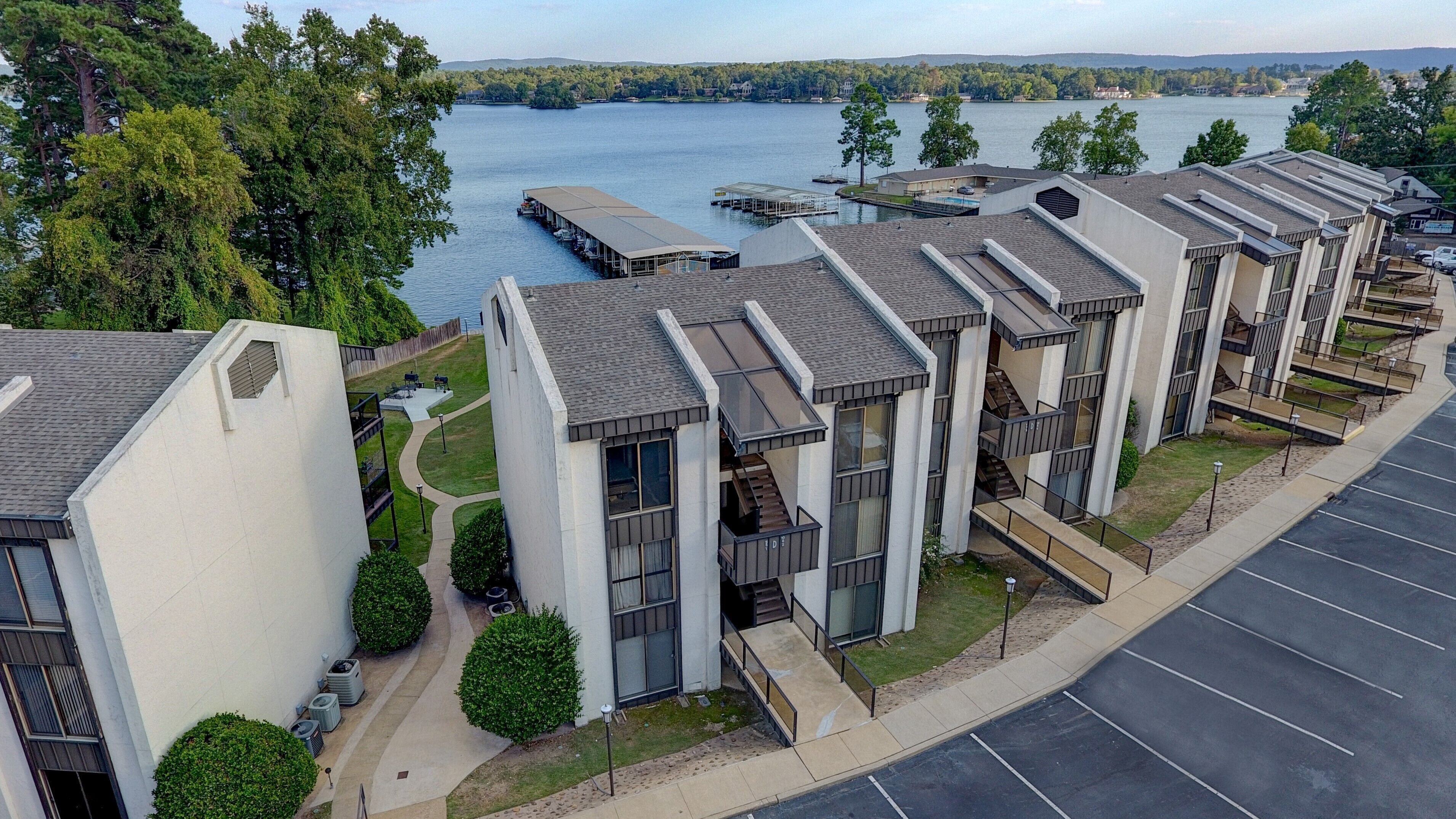 A modern apartment complex with a view of a lake, featuring multiple balconies and a parking area.
