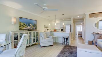 A spacious living area with a dining table, a sofa, a kitchen in the background, and a ceiling fan.