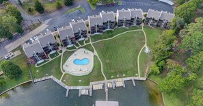 An aerial view of a residential complex with a central swimming pool, connected by a wooden dock.