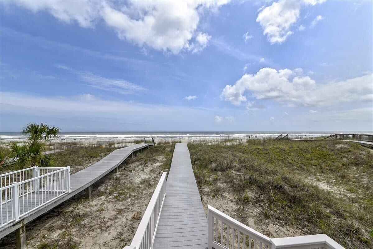 A wooden boardwalk leading to a beach with a clear sky and clouds.