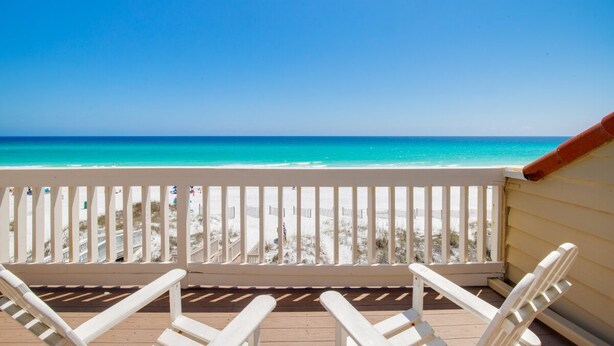 Eine Holzterrasse mit weißen Stühlen mit Blick auf einen Strand.