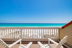 Eine Holzterrasse mit weißen Stühlen mit Blick auf einen Strand.