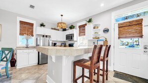 Una cocina moderna con armarios blancos, una isla central y un comedor con sillas de madera.