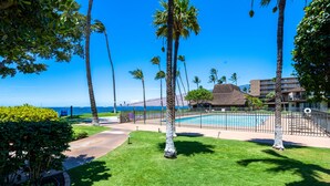 A pool area with palm trees, a thatched-roof building, and a view of the ocean. - Ma'alaea Surf Unit E4-2 BR Ground Floor Beachfront Condo, AC, Wi-Fi, Pool, TV (Kihei)
