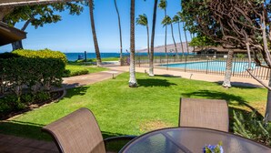 A patio with a glass table and chairs, a small flower vase, a swimming pool, and a view of the ocean. - Ma'alaea Surf Unit E4-2 BR Ground Floor Beachfront Condo, AC, Wi-Fi, Pool, TV (Kihei)