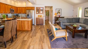 A spacious living area with a kitchen, dining area, and a gray sofa. - Ma'alaea Surf Unit E4-2 BR Ground Floor Beachfront Condo, AC, Wi-Fi, Pool, TV (Kihei)