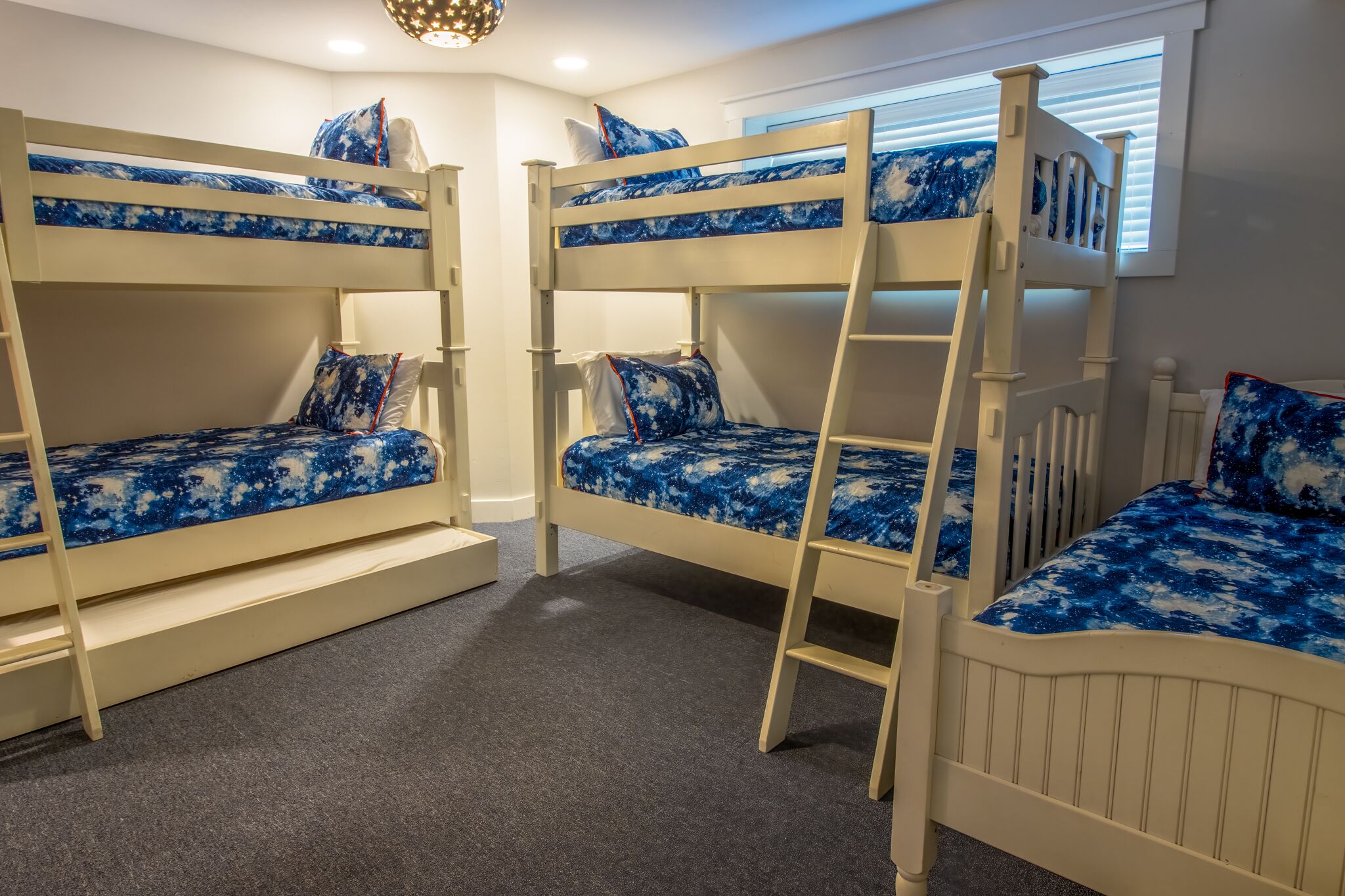 Une chambre avec des lits superposés, chacun équipé d’une échelle, et une fenêtre avec des stores.