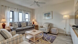 A living room with a sofa, armchairs, a coffee table, a ceiling fan, a TV, and a lamp. - DR 1309 – Getaway to this oceanfront condo with pool and direct beach access (Wrightsville Beach)
