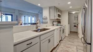 A modern kitchen with white cabinetry, a stainless steel refrigerator, and a microwave. - DR 1309 – Getaway to this oceanfront condo with pool and direct beach access (Wrightsville Beach)