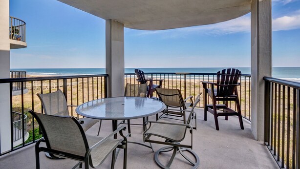 A balcony with a glass table and chairs, overlooking a beach. - DR 1309 – Getaway to this oceanfront condo with pool and direct beach access (Wrightsville Beach)