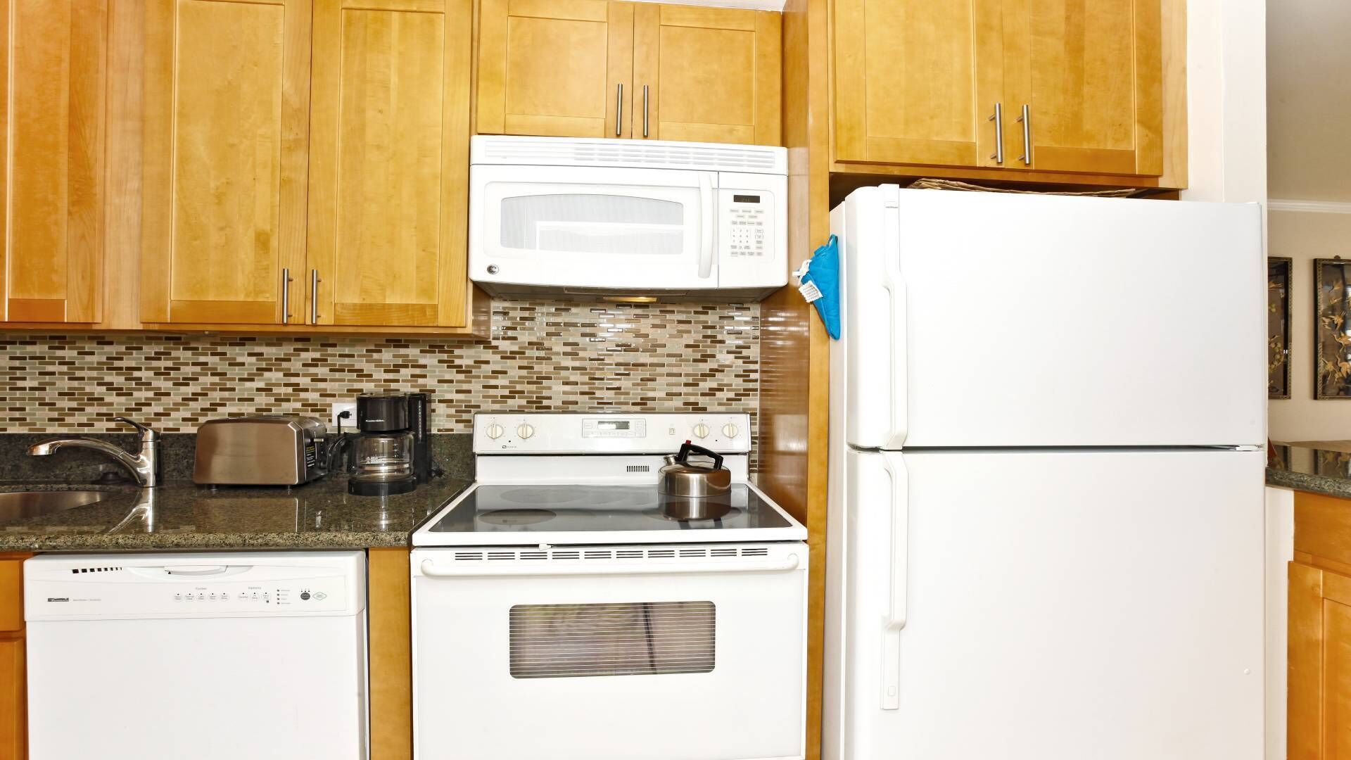 A kitchen with wooden cabinets, a microwave, a stove, a refrigerator, a dishwasher, and a coffee maker.