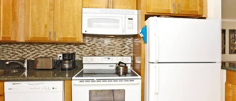 A kitchen with wooden cabinets, a microwave, a stove, a refrigerator, a dishwasher, and a coffee maker.