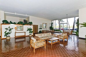 A spacious lobby with a tiled floor, a sofa set, a coffee table, and several potted plants.