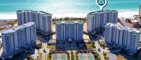 A high-rise hotel complex with multiple buildings, a central courtyard with tennis courts, and a beachfront view.