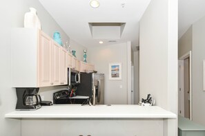 A compact kitchen with white cabinets, a stainless steel refrigerator, a coffee maker, and a microwave.