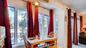 A dining area with a wooden table set for two, red curtains, and a view of trees outside. - Adorable Condo, Walking Distance To Everything. Including Pool/Hot Tub IC4 (Breckenridge)