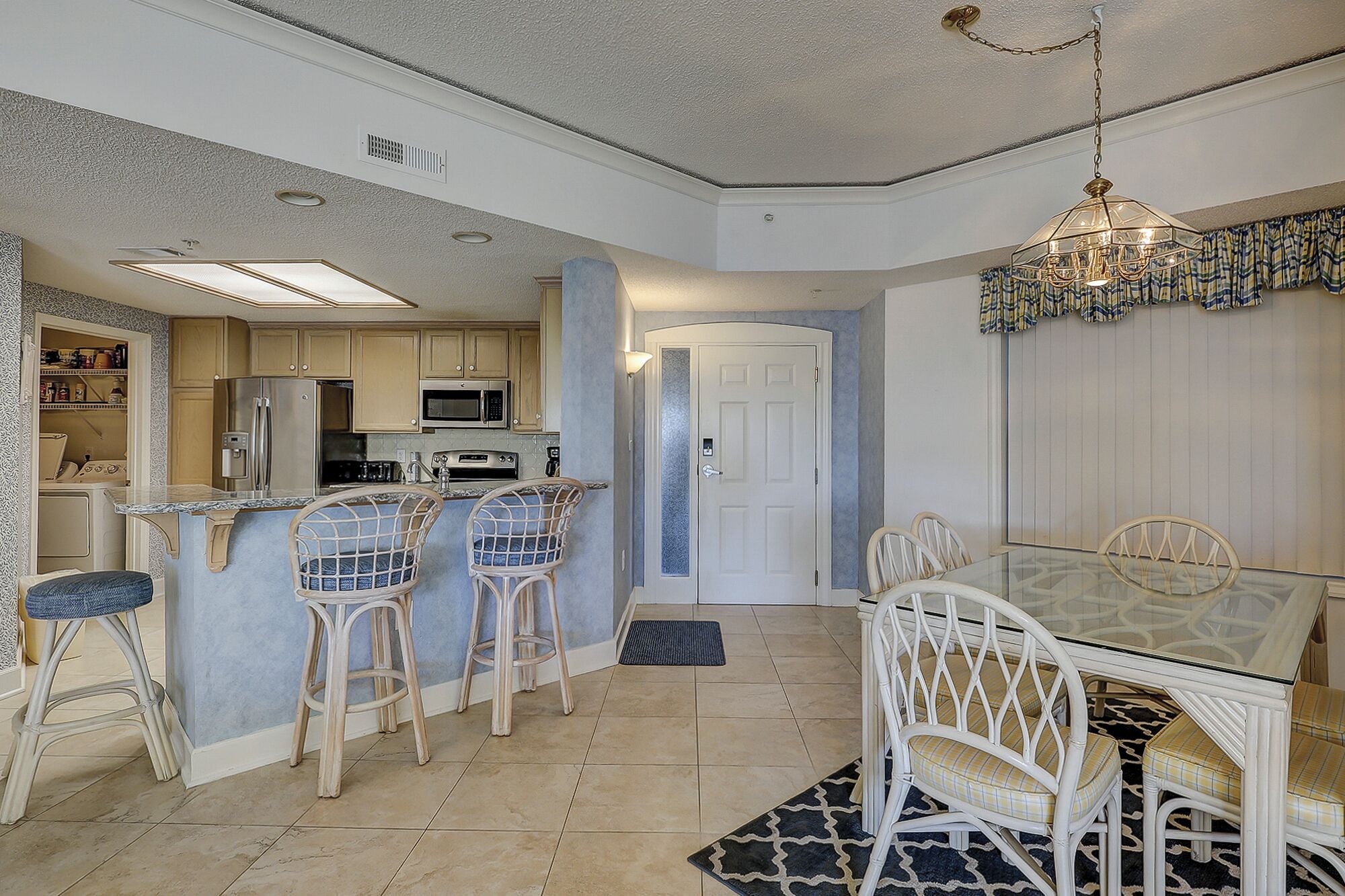 A compact kitchen with a dining area, featuring a refrigerator, microwave, and stove. There are bar stools and a dining table with chairs.