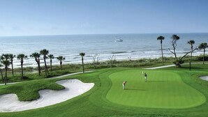 Ein Golfplatz mit Sandbunkern, Blick auf das Meer und ein Schiff in der Ferne.