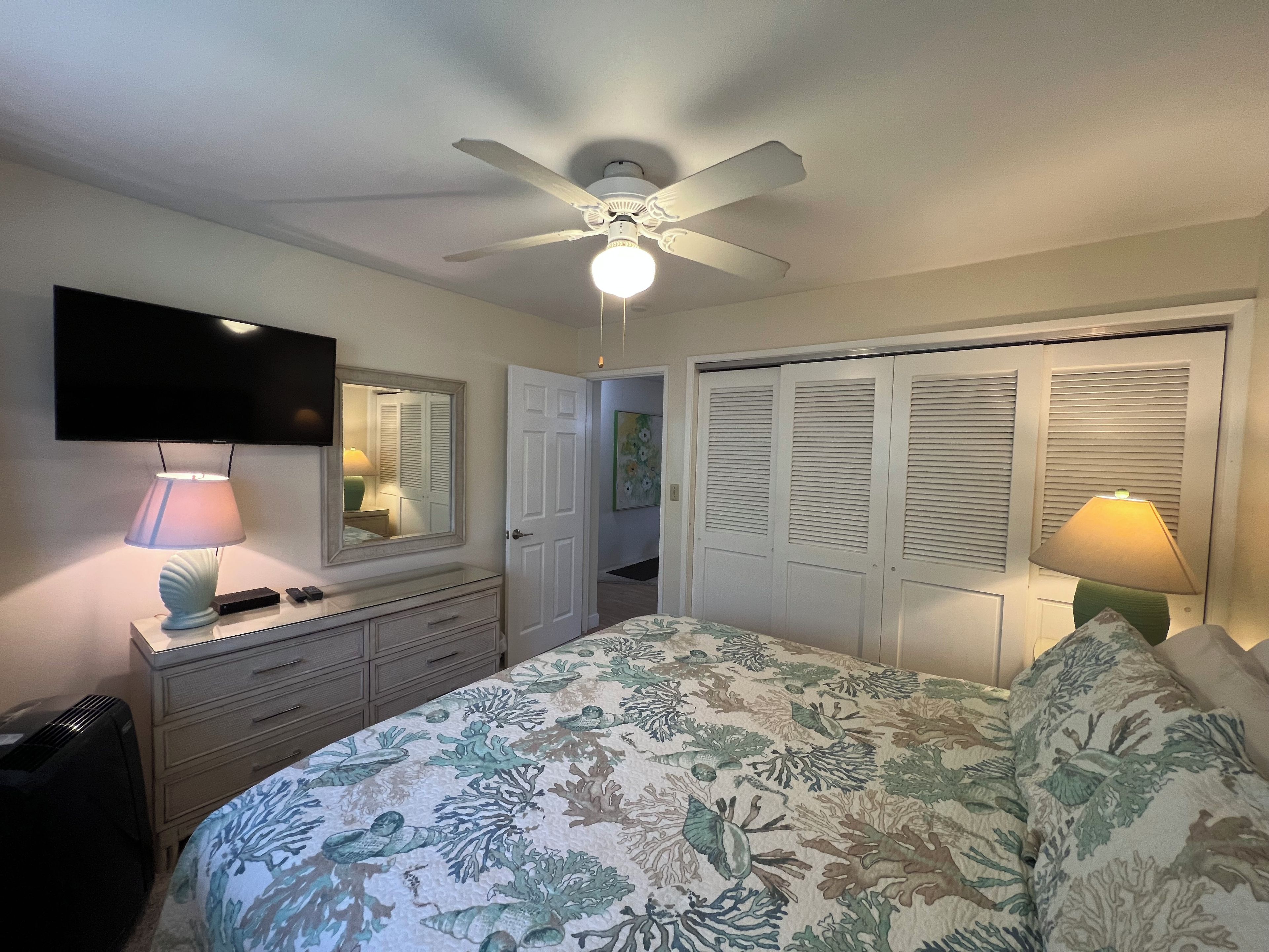 A bedroom with a bed, a ceiling fan, a TV, and a dresser.