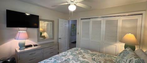 A bedroom with a bed, a ceiling fan, a TV, and a dresser.