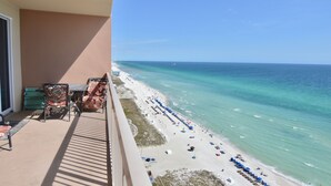 Ein Balkon mit Blick auf einen Strand, einem Tisch, Stühlen und einem grünen Koffer.