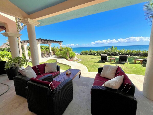 A covered outdoor seating area with wicker furniture, a pergola, and a view of the ocean.