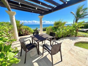 A covered outdoor seating area with a table and chairs, overlooking a scenic view of the ocean.