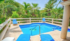 A pool area with a white fence, blue lounge chairs, and a clear blue pool.