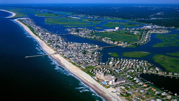 An aerial view of a coastal town with a beach, marina, and residential areas.