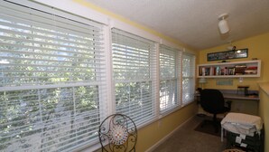 A room with large windows, a chair, a small table, a desk, and a bookshelf.